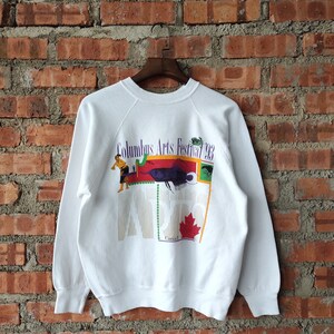 Könnte beinhalten: Weißer Pullover mit einem bunten Grafikdruck auf der Rückseite. Die Grafik zeigt einen Fisch, eine Person und den Text "Columbus Arts Festival 93".