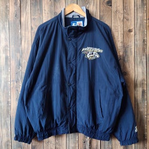 May include: A navy blue jacket with a Carolina Hurricanes logo on the front. The jacket has a zipper closure and a drawstring at the waist.