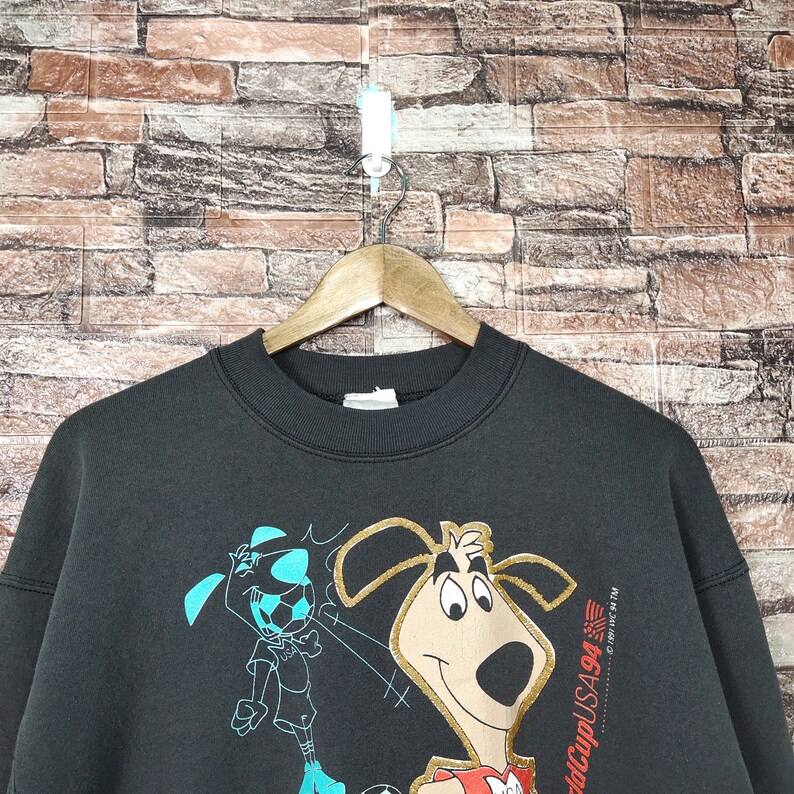 May include: Black sweatshirt with a cartoon dog and a soccer player graphic. The text "World Cup USA 94" is printed on the right side of the sweatshirt.