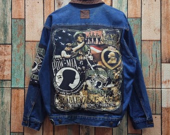 May include: A blue denim jacket with a brown collar and a large graphic print on the back. The print features a soldier, a motorcycle, the text "ALL GAVE SOME," "POW MIA," "MYRTLE BEACH SC," and "SOME GAVE ALL AND THEY'LL RIDE WITH US."