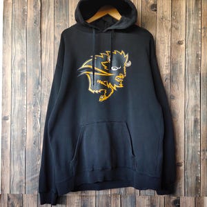 May include: Black hooded sweatshirt with a front kangaroo pocket. The sweatshirt features a yellow and black graphic of a bison. The hoodie is hanging on a wooden hanger against a wooden background.