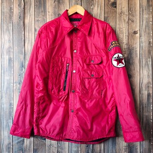 May include: A bright pink jacket with a collared neckline and multiple pockets. The jacket features a Texaco patch with a red star and a vintage motors patch. The jacket is button-down and has a zipper pocket.