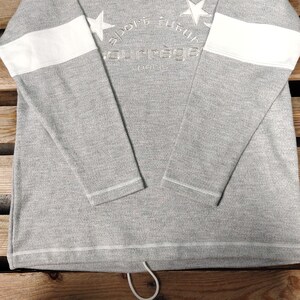 May include: Gray long-sleeve sweatshirt with white stripes on the sleeves and a white embroidered logo that says "sport futur" and "courr&egrave;ges paris".