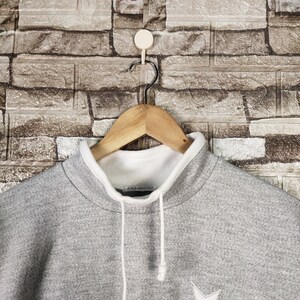 May include: Gray sweatshirt with a white mock neck and a white drawstring. The sweatshirt has a small white star on the front.