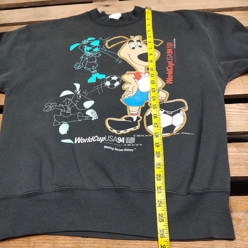 May include: Black sweatshirt with a graphic print of cartoon dogs playing soccer. The text "WorldCup USA94" and "Making Soccer History" is printed on the sweatshirt.