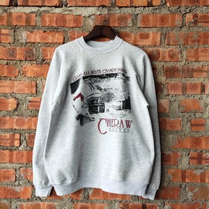 May include: Grey sweatshirt with a maroon print of a football helmet and a stadium scene. The text reads "Class AAA State Championship" and "Cheraw Braves".