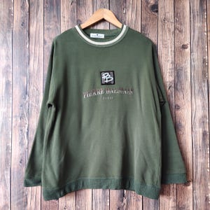 May include: A green sweatshirt with a white crew neck and a white embroidered logo that says "Pierre Balmain Paris" with a small square logo featuring the letters "BB" in the center.