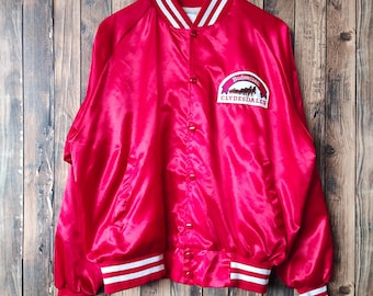May include: A red satin bomber jacket with white stripes on the collar, cuffs, and waistband. The jacket has a button closure and features a Budweiser Clydesdales logo on the left chest.