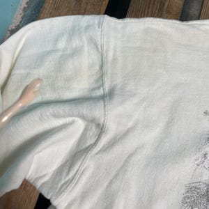 May include: White cotton sweatshirt with a smooth texture. The sweatshirt has a slight sheen and is folded in half.