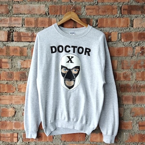 May include: Gray sweatshirt with a black and white illustration of a masked wrestler. The text "DOCTOR X" is printed in black above the illustration.