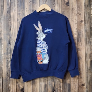 Op de afbeelding: Een donkerblauwe trui met een afbeelding van Bugs Bunny die skateboardt. De afbeelding bevat de tekst "Los Angeles Skate".