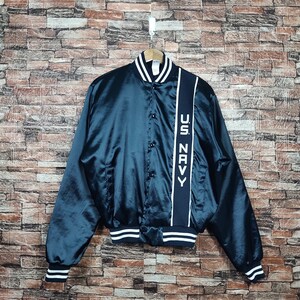 Könnte beinhalten: Eine dunkelblaue Satin-Bomberjacke mit weißen und schwarzen Streifen an den Säumen. Die Jacke hat einen Druckknopfverschluss und einen vertikalen Streifen auf der rechten Seite mit dem Text "U.S. NAVY" in Weiß.