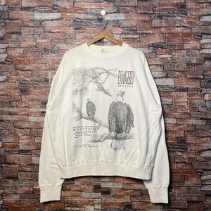 May include: White crewneck sweatshirt with a graphic print of two bald eagles in a forest setting. The text "Endangered Species" and "North American Bald Eagle" is printed on the sweatshirt.