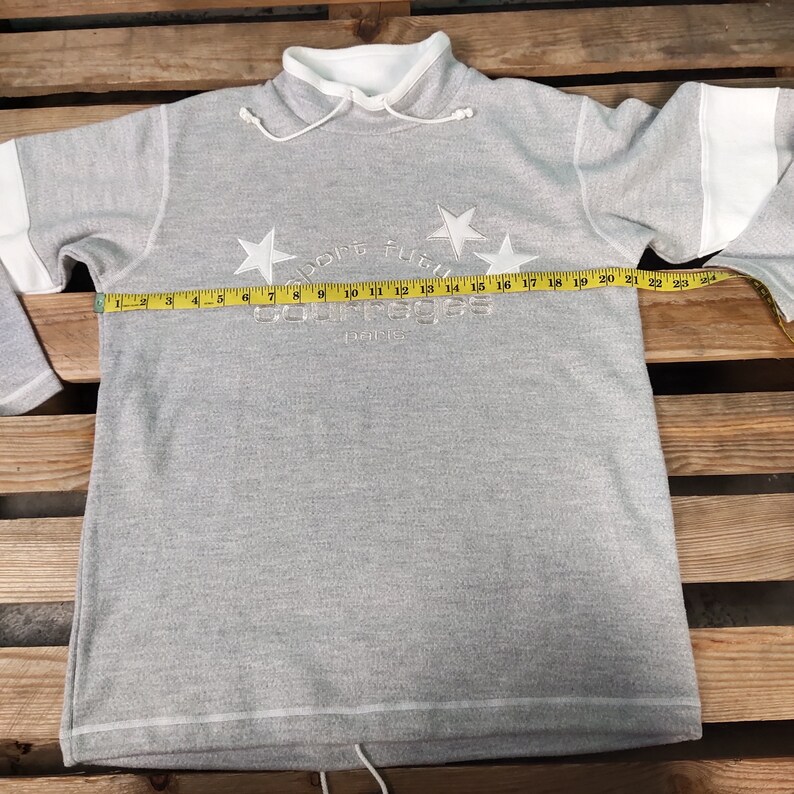 May include: Gray sweatshirt with a white collar and white trim on the sleeves. The sweatshirt has a white embroidered logo that says "Courage" with stars and the text "Paris".