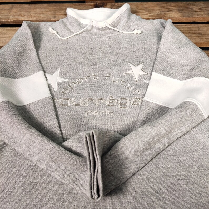May include: Gray sweatshirt with white stripes on the sleeves. The sweatshirt has a star and the text "sport futur" and "courr&egrave;ges paris" embroidered on the front.