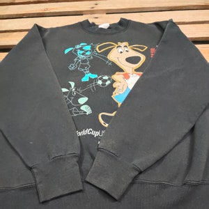 May include: Black sweatshirt with a graphic print of cartoon dogs playing soccer. The text "World Cup USA 94" is printed on the bottom of the sweatshirt.