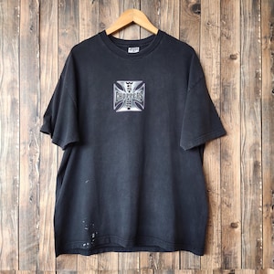 以下が含まれることがあります： 「West Choppers」の文字が四角いデザインでプリントされた黒いTシャツ。木製のハンガーに掛けられ、木製の背景に配置されています。生地は少し色あせたように見えます。