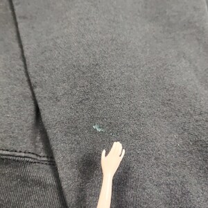 May include: Close-up of a black fabric surface with a small light blue stain.
