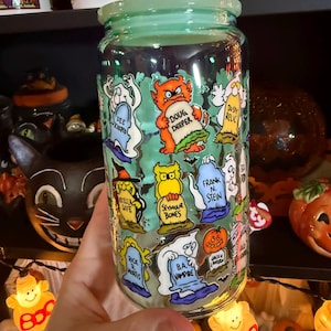 Peut inclure: Un bocal en verre transparent avec un couvercle vert clair, d&eacute;cor&eacute; de personnages de dessins anim&eacute;s d'Halloween sur des pierres tombales. Le bocal pr&eacute;sente des personnages comme "Doug Deeper" et "B.A. Vampire".