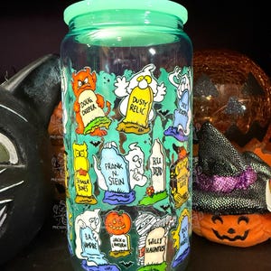 Peut inclure: Un bocal en verre transparent avec un couvercle vert, d&eacute;cor&eacute; de personnages de dessins anim&eacute;s et de pierres tombales sur le th&egrave;me d'Halloween. Le bocal pr&eacute;sente des images de fant&ocirc;mes, de citrouilles et de chauves-souris, avec des phrases comme "Doug Deeper" et "Willy Hauntus".