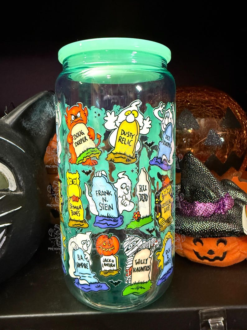 Peut inclure: Un bocal en verre transparent avec un couvercle vert, d&eacute;cor&eacute; de personnages de dessins anim&eacute;s et de pierres tombales sur le th&egrave;me d'Halloween. Le bocal pr&eacute;sente des images de fant&ocirc;mes, de citrouilles et de chauves-souris, avec des phrases comme "Doug Deeper" et "Willy Hauntus".