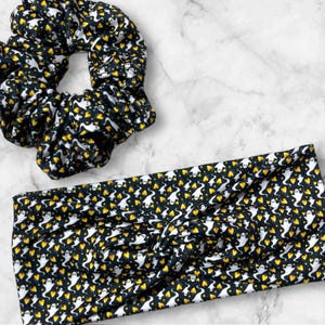 May include: A black and white headband and scrunchie set with a pattern of white ghosts and yellow hearts.