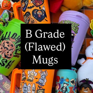 May include: A collection of Halloween-themed plastic mugs in orange, green, purple, and teal, featuring various graphic prints of pumpkins, ghosts, and tombstones, alongside a plush Garfield toy wearing a red devil cape and a small ghost figure.