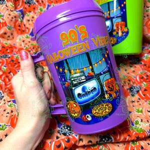 Op de afbeelding: Een paarse plastic beker met deksel voorzien van de tekst 90's HALLOWEEN VIBES en een afbeelding van een televisiescherm met het woord CASPER, een pompoenemmer, een pizza en een frisdrankblikje, met lichtsnoeren op de achtergrond.