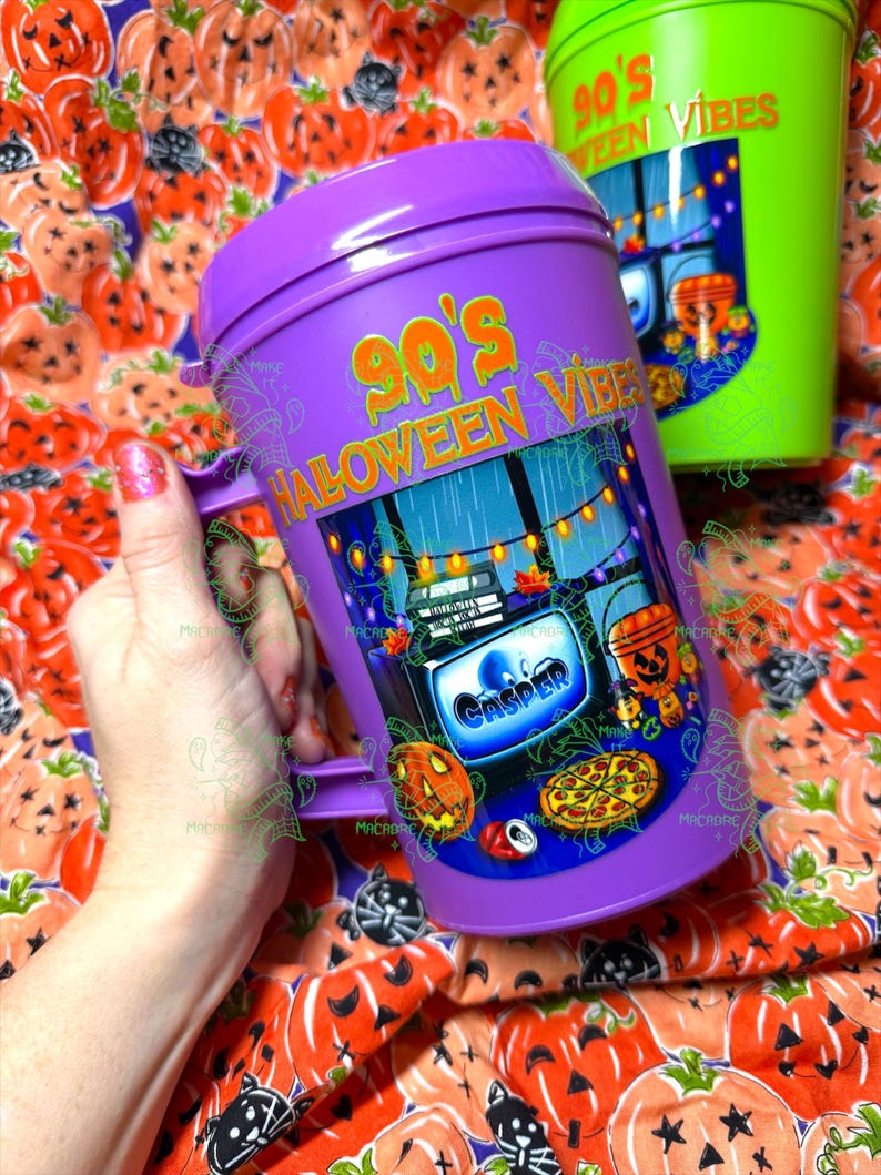 Op de afbeelding: Een paarse plastic beker met deksel voorzien van de tekst 90's HALLOWEEN VIBES en een afbeelding van een televisiescherm met het woord CASPER, een pompoenemmer, een pizza en een frisdrankblikje, met lichtsnoeren op de achtergrond.