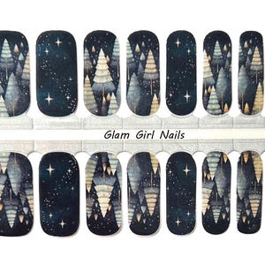 May include: Nail polish wraps with a winter forest design. The wraps feature a dark blue background with white and gold trees and stars. The text "Glam Girl Nails" is printed on the sheet.