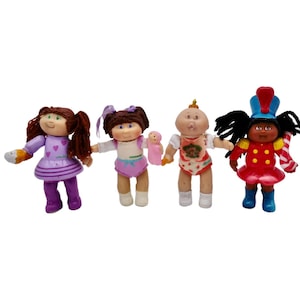 May include: Four Cabbage Patch Kids dolls, each with a different outfit and hairstyle. The dolls are all smiling and have rosy cheeks. One doll is wearing a purple dress with hearts, another is wearing a blue and white striped dress, another is wearing a red and white striped dress, and the last doll is wearing a red and white striped dress with a blue hat.