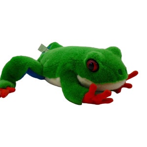 May include: Green plush frog toy with red feet and a white belly. The frog has large, black eyes and a wide, toothy grin.