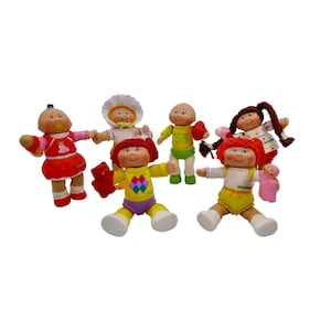 May include: A group of six Cabbage Patch Kids dolls in various outfits. The dolls are all wearing different colored clothes and have different hairstyles. Some of the dolls are holding accessories, such as a teddy bear, a football, and a baby doll.