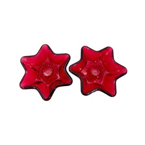 May include: Two red glass candle holders shaped like stars. The holders have a small hole in the center for a candle.