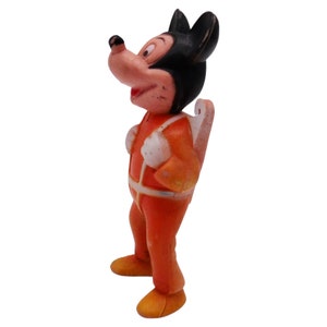 May include: A vintage plastic figurine of Mickey Mouse wearing an orange jumpsuit and a jetpack. The figurine is in good condition with some minor wear and tear.