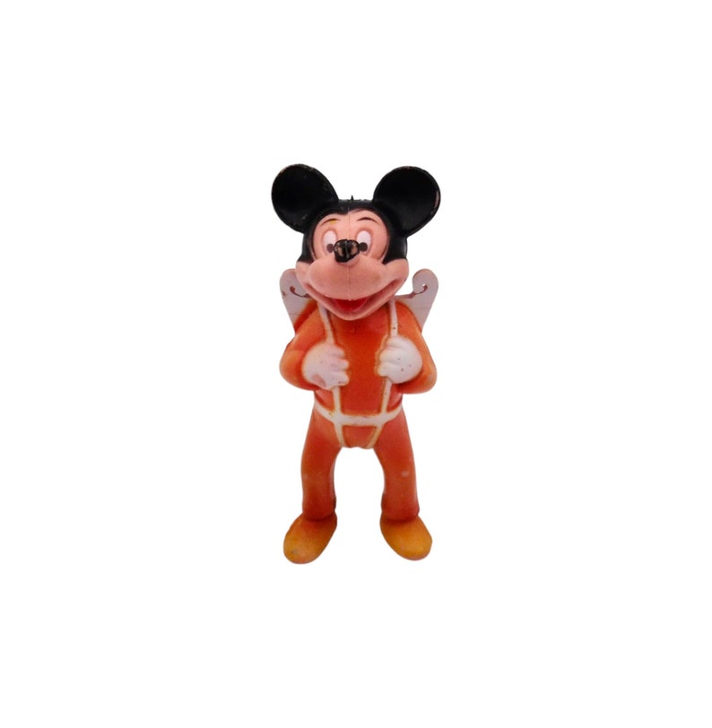 May include: A small plastic figurine of Mickey Mouse wearing an orange jumpsuit and a white parachute. He has black ears and a black nose.