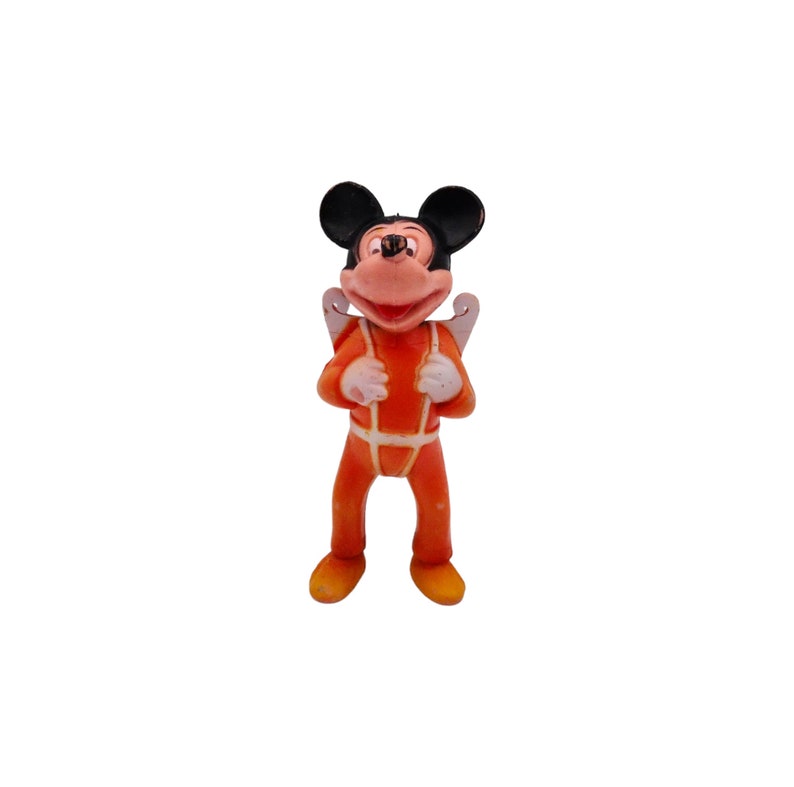 May include: A small plastic figurine of Mickey Mouse wearing an orange jumpsuit with white accents and a white parachute on his back.