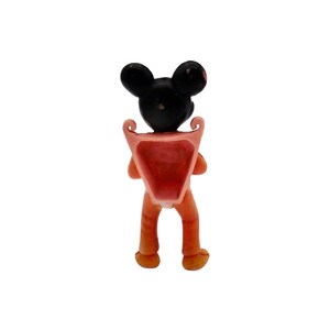 May include: A small plastic figurine of Mickey Mouse wearing a pink backpack. The figurine is facing away from the camera, showing the back of the backpack.