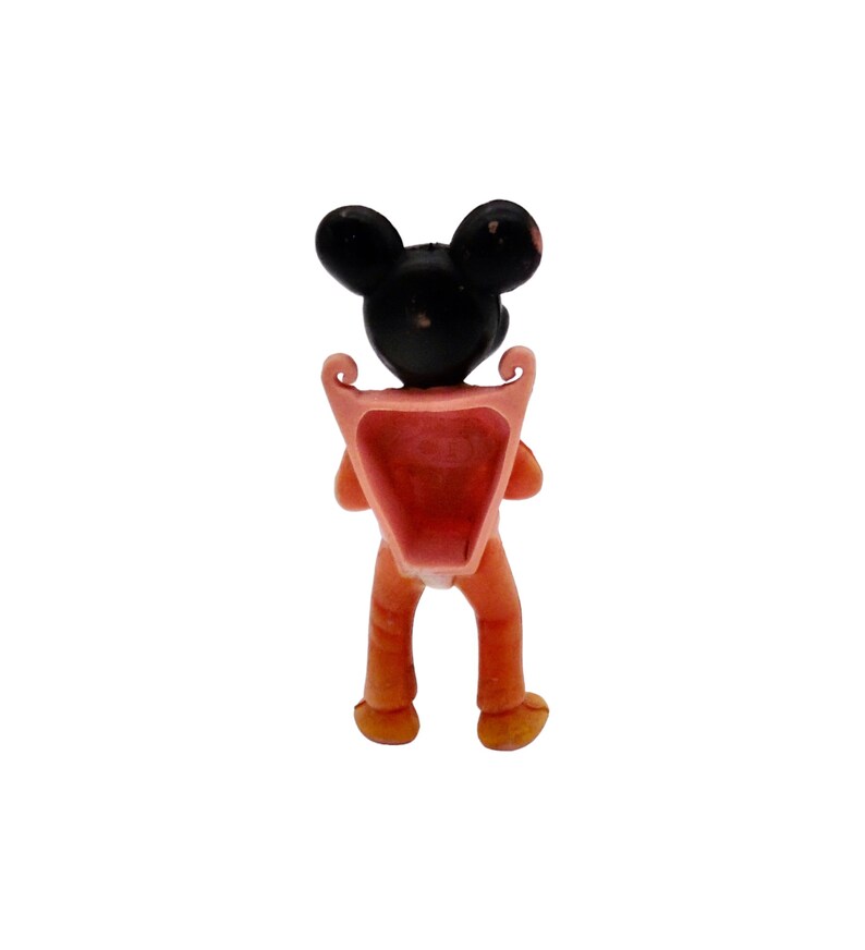 May include: A small plastic figurine of Mickey Mouse wearing a pink backpack. The figurine is facing away from the camera, showing the back of the backpack.