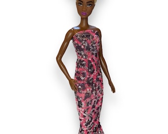 May include: A black doll with blonde hair styled in a high bun wearing a pink and black sequined gown.