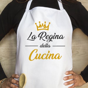 Peut inclure: Tablier blanc avec une couronne dorée et le texte "La Regina della Cucina" en lettres noires et dorées.