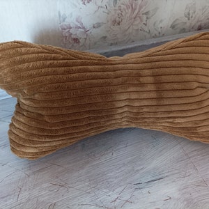 Könnte beinhalten: Ein braunes Kissen aus Cord in Knochenform. Das Kissen ist weich und flauschig, perfekt zum Kuscheln.