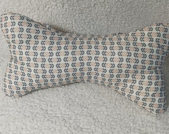 May include: A white and grey patterned neck pillow with a geometric design. The pillow is shaped like a bone and is made of soft fabric.