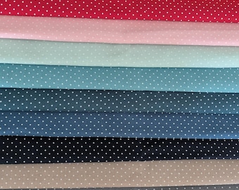 May include: A collection of various colored fabrics, each featuring a repeating pattern of small white polka dots. Colors include yellow, red, pink, light blue, teal, navy, dark blue, tan, gray, and black. The fabrics are neatly stacked, showcasing the range of available colors.