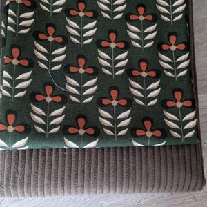 Könnte beinhalten: Ein gefaltetes Stoffobjekt mit floralem Muster. Die obere Schicht zeigt ein dunkelgrünes Design mit orangefarbenen und weißen Blumen. Die untere Schicht ist ein brauner Stoff im Cord-Stil. Es könnte sich um ein Kissen oder ein ähnliches Textil handeln.