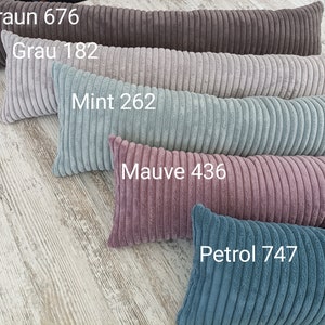 Peut inclure: Cinq longs coussins rectangulaires de différentes couleurs. Les coussins sont faits d'un tissu doux et côtelé. Les couleurs sont le brun, le gris, le vert menthe, le mauve et le bleu sarcelle. Les coussins sont étiquetés avec leur couleur et un numéro.