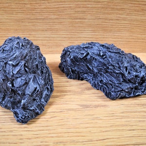 Op de afbeelding: Twee grijze, getextureerde, rotsachtige objecten. De rotsen zijn gemaakt van een ruw, gegoten materiaal en hebben een licht onregelmatig oppervlak.