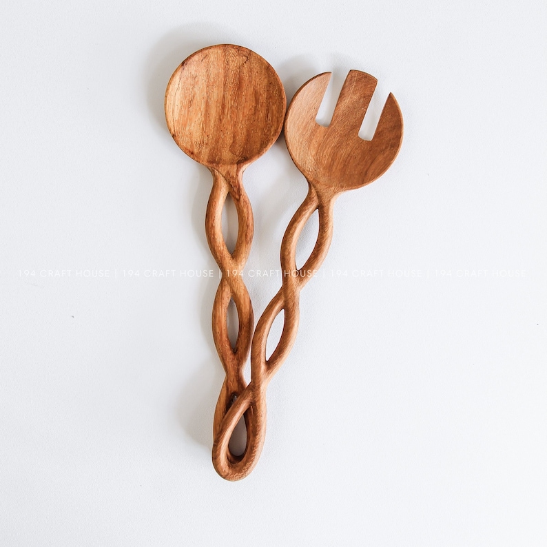 May include: A set of two wooden salad servers with a twisted design. The servers are made of natural wood and have a light brown color.