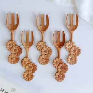 May include: Set of five wooden forks with carved daisy details. The forks are brown and have two prongs.