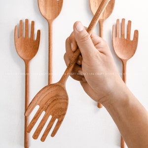 May include: A set of five wooden kitchen utensils with a hand-shaped design. The utensils are made of natural wood and have a warm brown color.